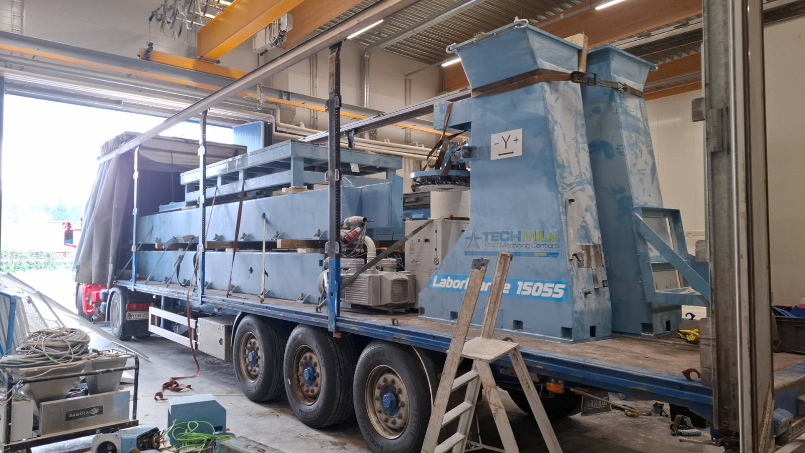 Raskaan koneen lastaus hallissa siniselle lavettiautolle